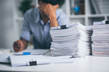 A stressed man with piles of paper in front of him.