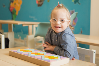 small smiling child with down syndrome in a classroom
