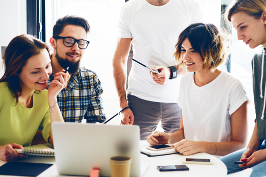 A group of people gathering around a laptop smiling 