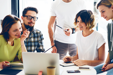 A group of people gathering around a laptop smiling