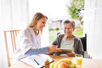 female care worker sitting together with an elderly resident of a care home, looking at the screen of a tablet