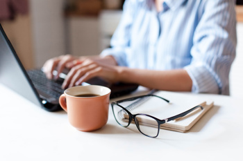 Person working from home, with a coffee and pair of glasses resting on the desk