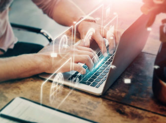 Close-up of a pair of hands typing something on a laptop. Hovering over the laptop there are a few white icons displaying a globe, a clock, and a suitcase.