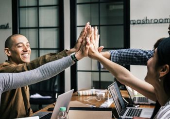 A group of people on laptops high-fiving