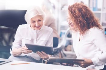 two young women having a conversation inside an office and looking at the screen of a tablet